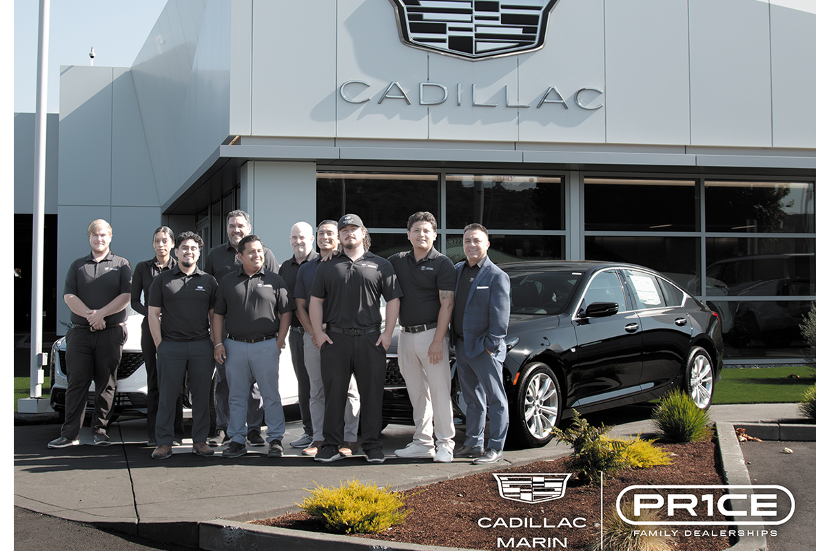 The Cadillac team, with two luxury cars behind them, pose in front of one of the Cadillac offices
