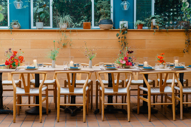 A long table surrounded by chairs, featuring a decorative arrangement of flowers on top.