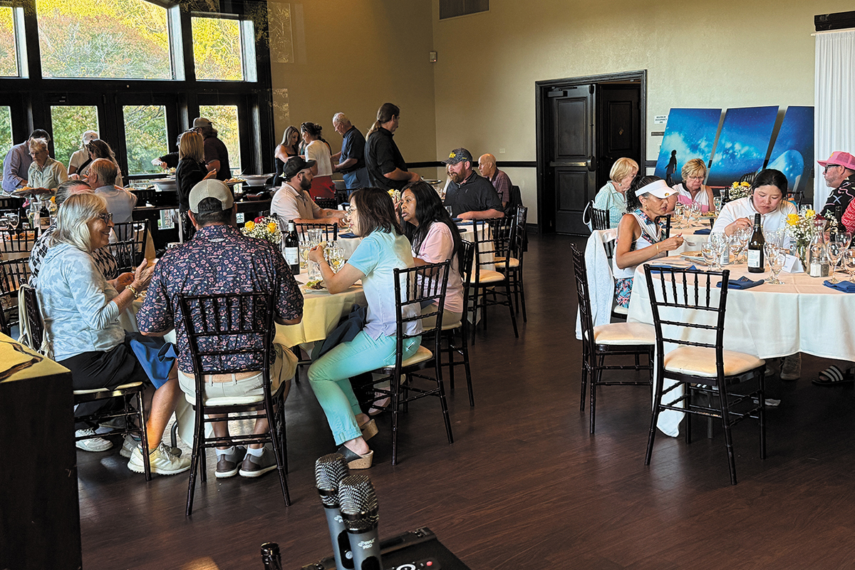 A diverse group of people sitting at tables in a room, interacting and sharing ideas in a collaborative environment.