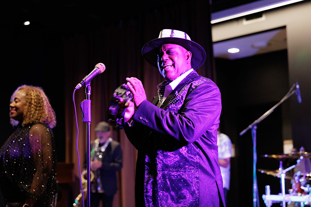 A man in a suit and hat passionately sings into a microphone on stage.