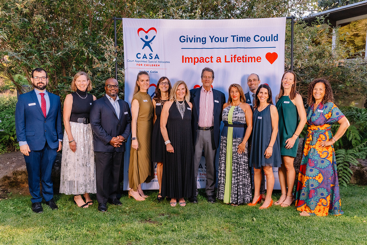 A group of people stands in front of a banner that reads "Giving Your Time Could" in a community event setting.