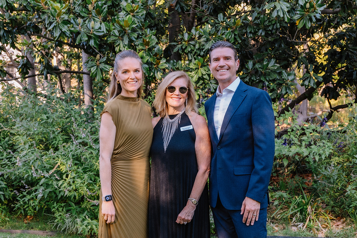 Three people standing together in a lush garden, surrounded by vibrant flowers and greenery.