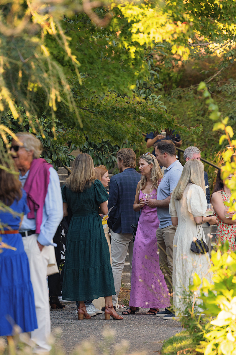 A group of people gathered around a large tree, engaging in conversation and enjoying the outdoor setting.