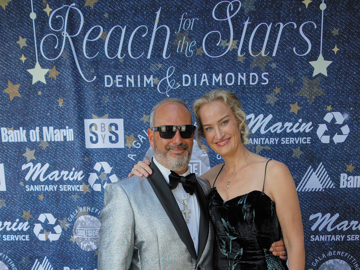 A man and woman pose together in front of a "Reach for the Stars" banner, smiling.