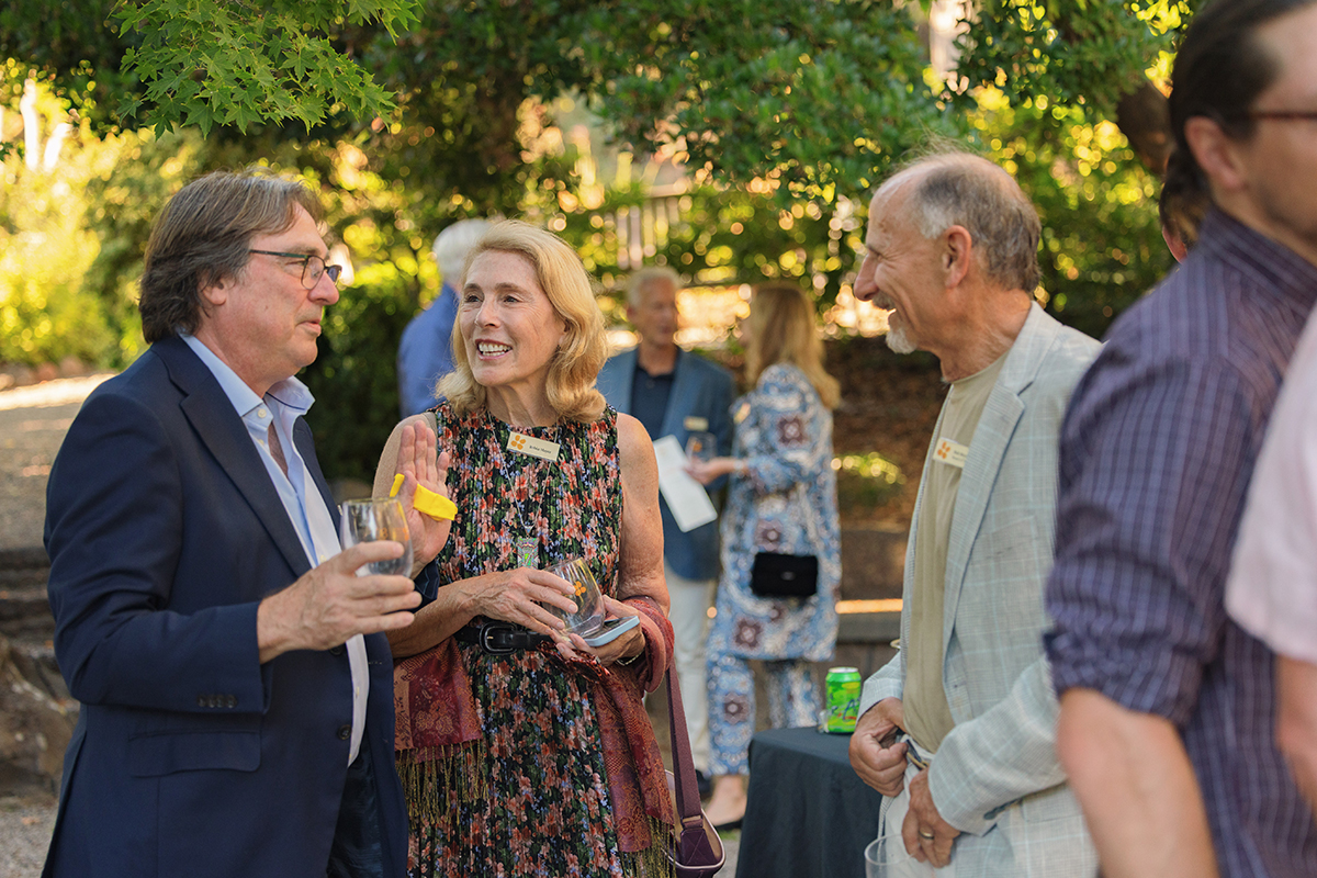 A group of people engaged in conversation while holding drinks at an outdoor event.