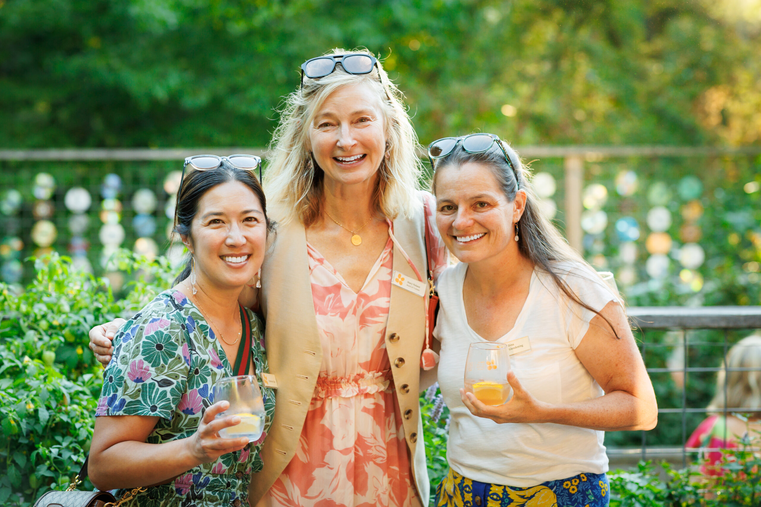 Three women stand and hold drinks.