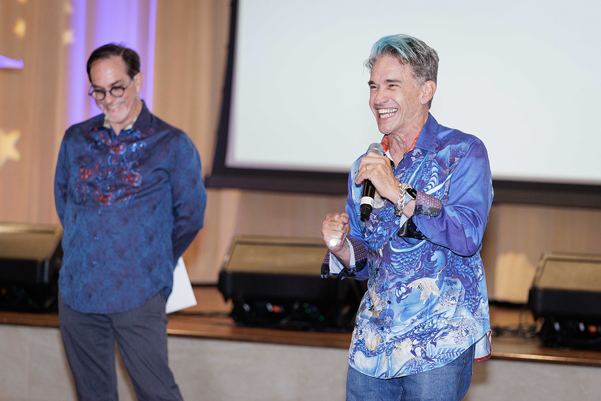 Two men in blue shirts and jeans are smiling at the camera, exuding a friendly and cheerful attitude.
