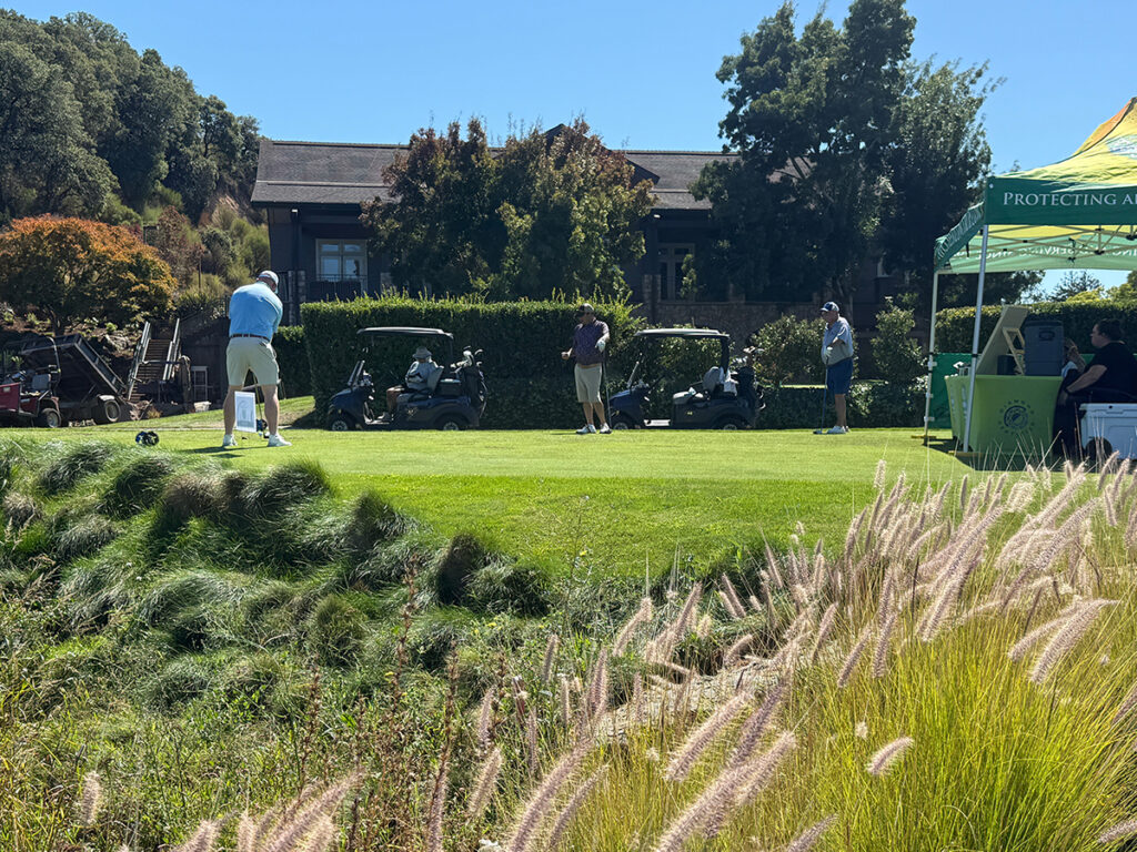 A scenic golf course featuring players in action and several tents set up for an event.