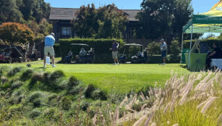 A scenic golf course featuring players in action and several tents set up for an event.