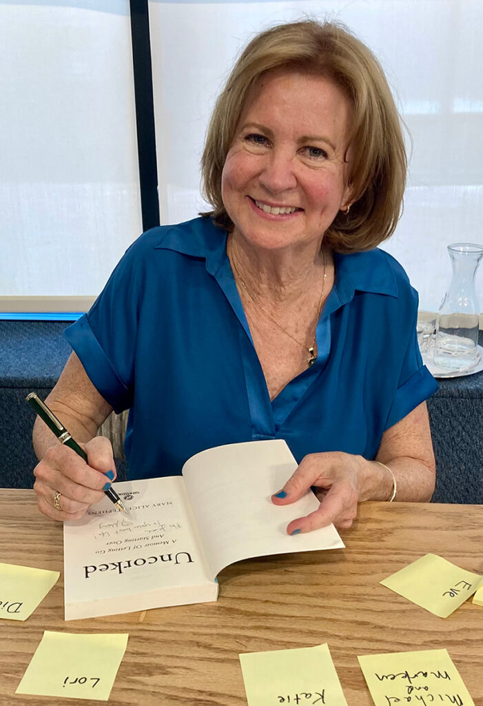 A woman sitting at a table covered with colorful sticky notes, signing a book.