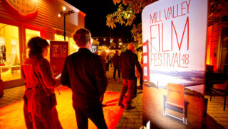 A red light is illuminated as pedestrians walk past a red sign on the street.