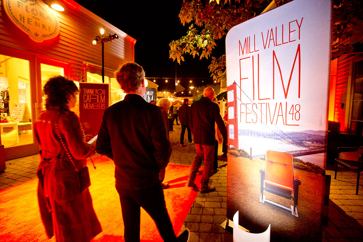 A red light is illuminated as pedestrians walk past a red sign on the street.