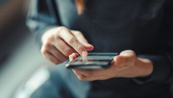A woman looks at her cell phone while holding it in her right hand, appearing focused on the screen.
