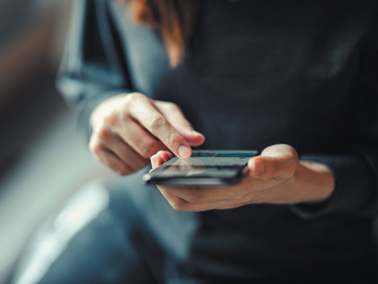 A woman looks at her cell phone while holding it in her right hand, appearing focused on the screen.