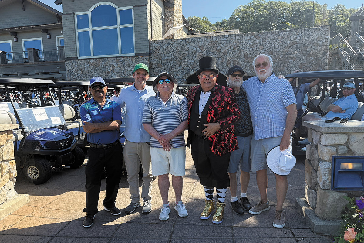 A group of men smiling and posing together for a photo on a sunny golf course.