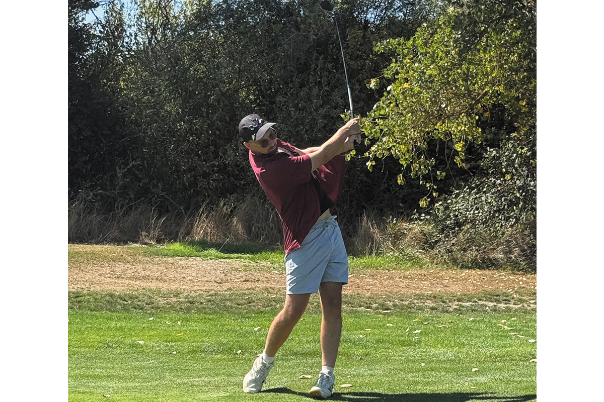 A man in a maroon shirt preparing to hit a golf ball on a sunny day.