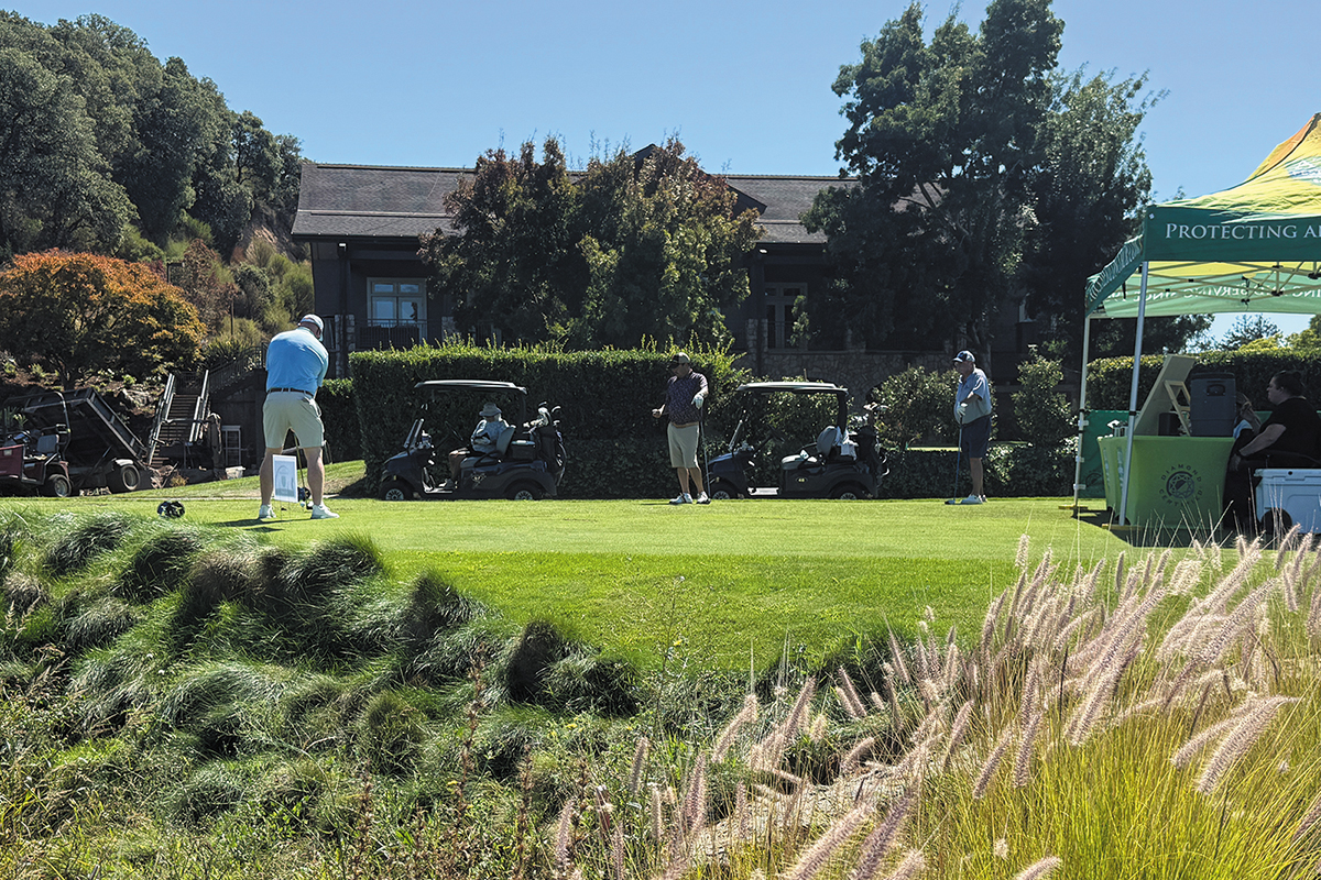 A scenic golf course featuring players in action and several tents set up for an event.