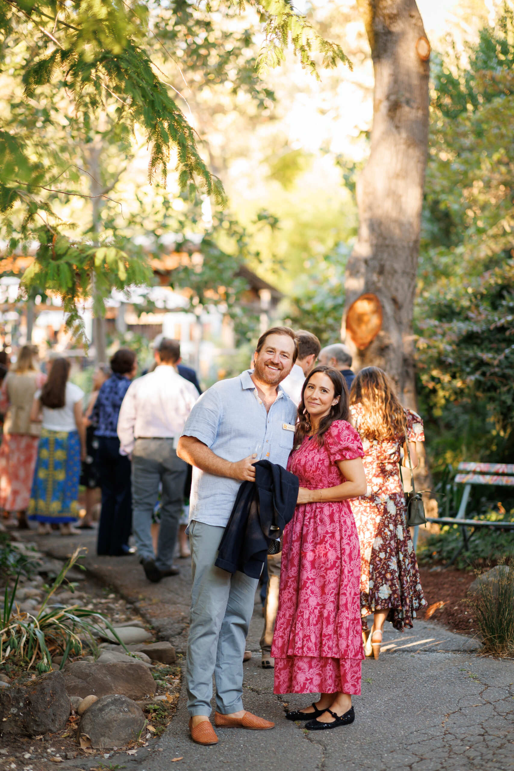 A couple stands amidst trees and other guests.