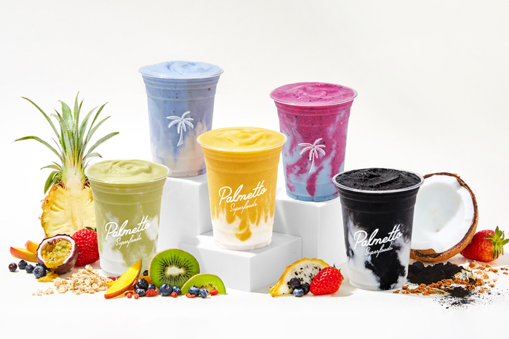 Various smoothies of vibrant colors are posed with pieces of fruit around.