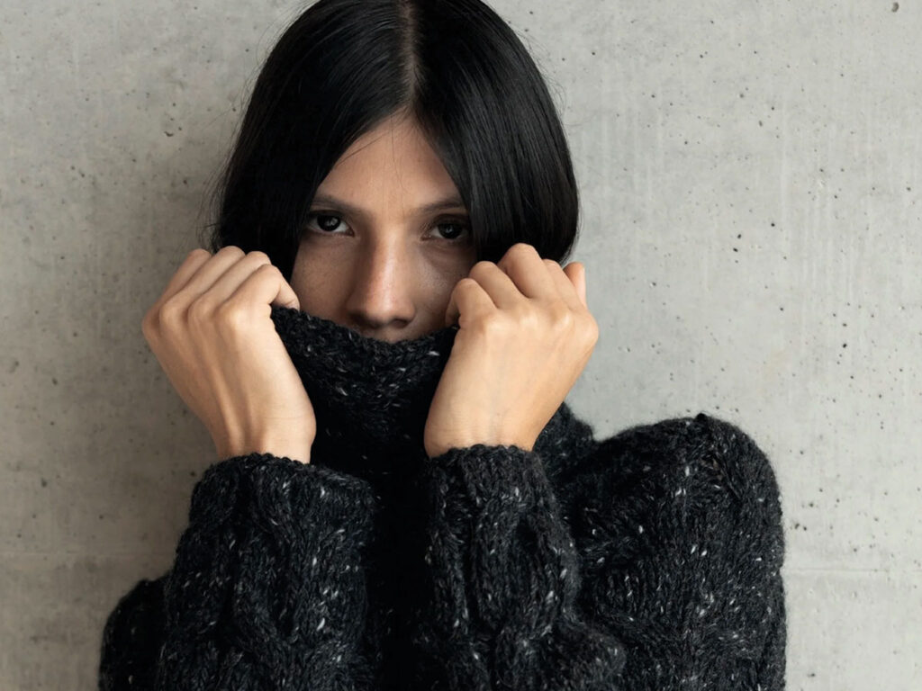 A woman wearing a black sweater covers her face, suggesting introspection or a desire for privacy.