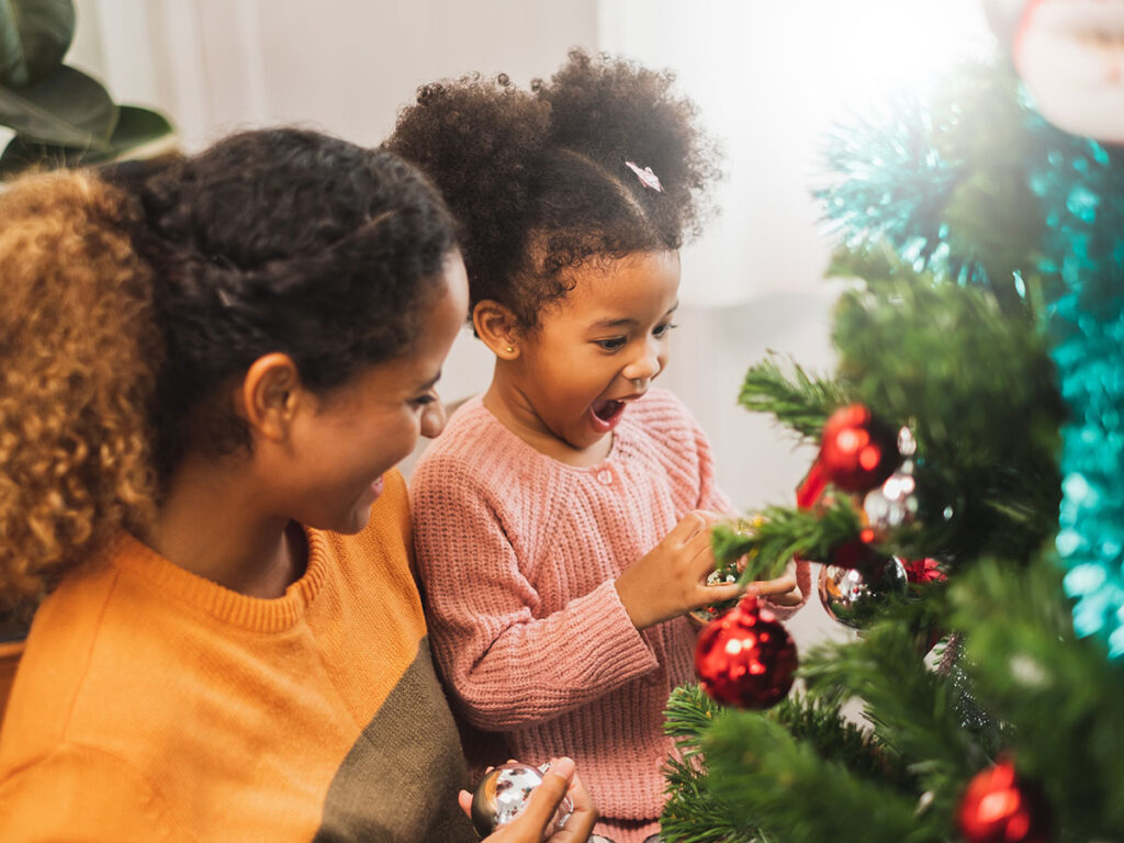 A mother and daughter joyfully decorating a Christmas tree with colorful ornaments and twinkling lights.