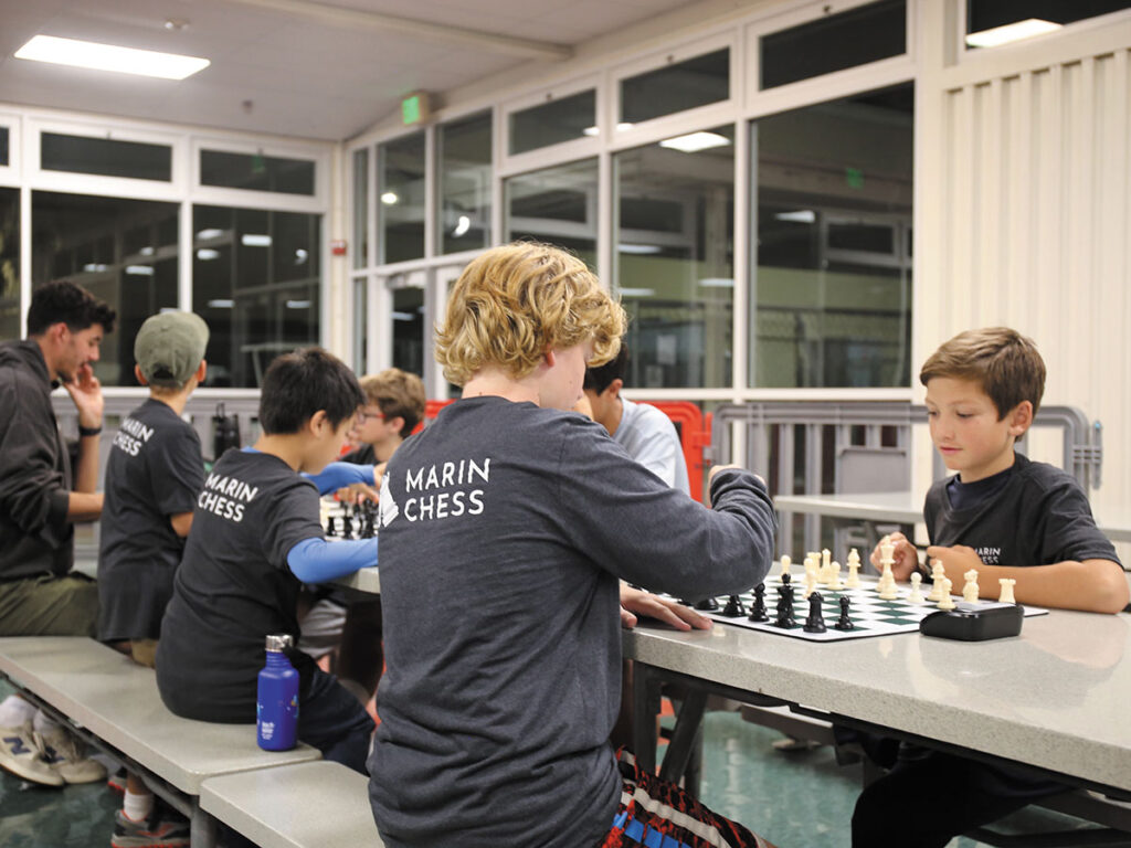 A table with boys playing chess, each boy intently considering his next move in the game.