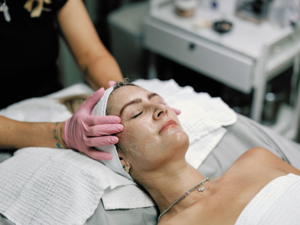 A woman receiving a facial treatment at a serene spa, relaxing on a treatment bed with soothing ambiance around her.