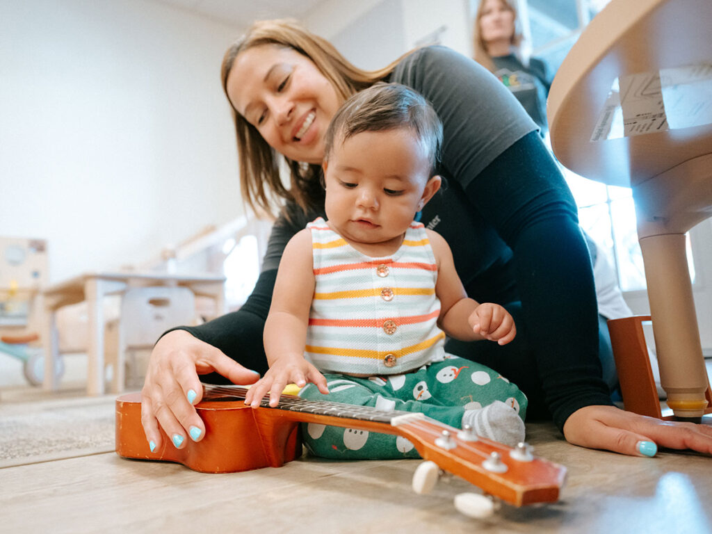 A woman and a baby joyfully playing together with a ukulele, sharing a moment of music and laughter.