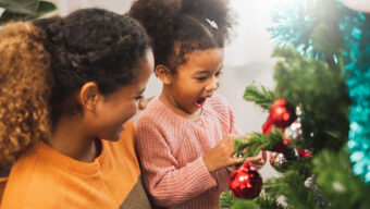 A mother and daughter joyfully decorating a Christmas tree with colorful ornaments and twinkling lights.