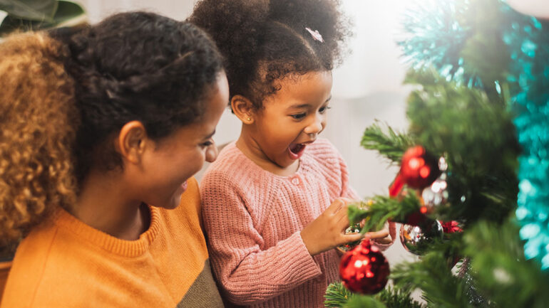 A mother and daughter joyfully decorating a Christmas tree with colorful ornaments and twinkling lights.