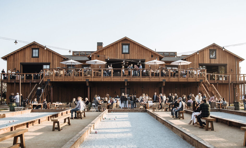 A beautifully decorated barn hosting a wedding reception, with tables set and guests mingling in a rustic ranch setting.