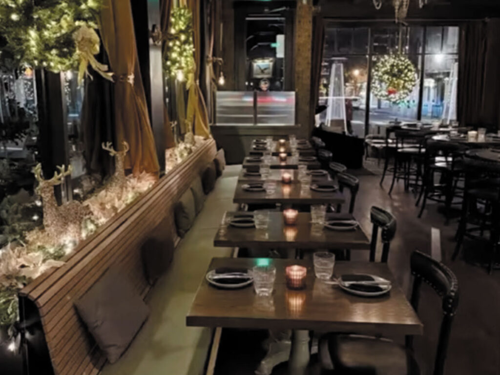 A warmly lit restaurant with tables and chairs, decorated with twinkling Christmas lights for a festive atmosphere.