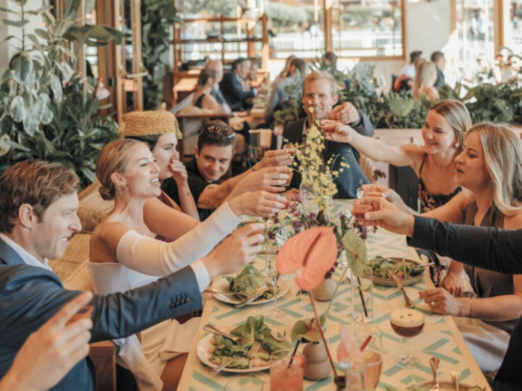A group of people raising glasses in a toast at a restaurant, celebrating together in a joyful atmosphere.