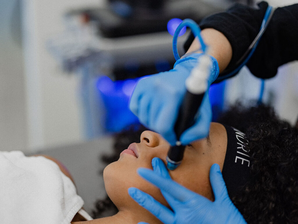 A woman receives a facial treatment from a professional dermatologist in a salon setting.