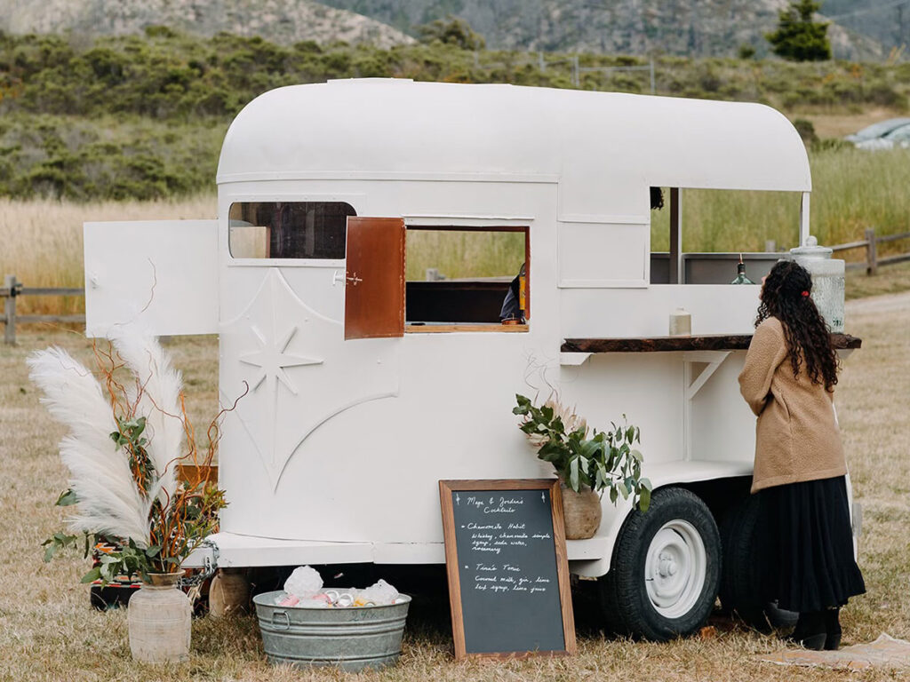 A woman stands beside a white trailer, smiling and dressed in casual outdoor attire.