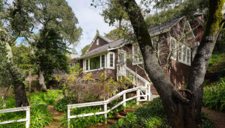 A charming house bordered by a white fence, with a pathway guiding visitors to the entrance.