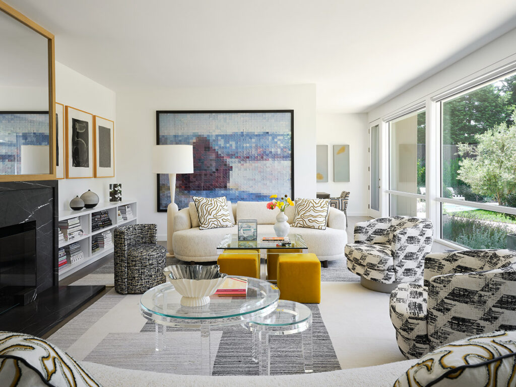 A modern living room with a white sofa, patterned chairs, and yellow ottomans. Large windows, abstract artwork, and a glass coffee table add elegance.
