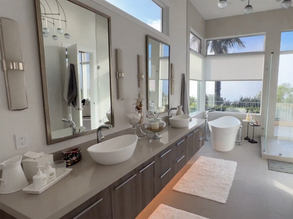 Luxurious bathroom with floor-to-ceiling windows, modern sinks, a freestanding tub, and minimal decor. Natural light creates an airy, serene ambiance.