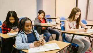 Four students sitting in a classroom, each focused on their phones.