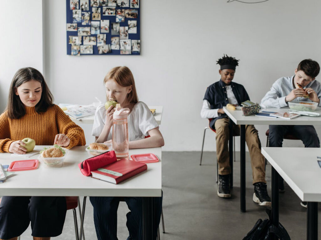 Four students sit at desks eating lunch.