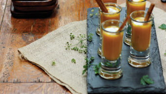 A platter with six shot glasses filled with butternut and apple soup.