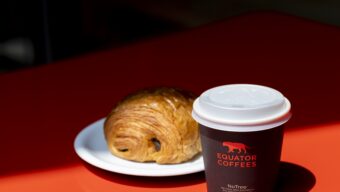 A croissant sits beside a cup of coffee on a red table.