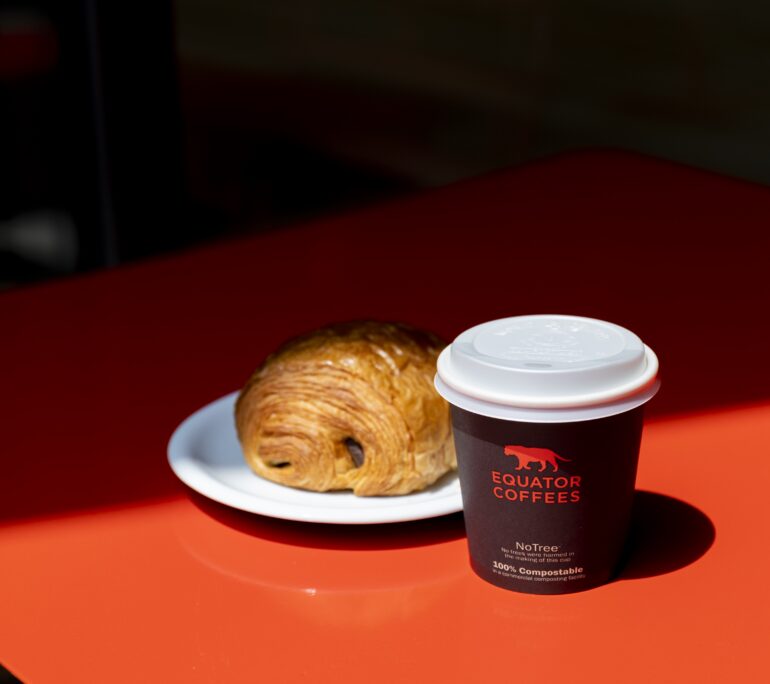 A croissant sits beside a cup of coffee on a red table.