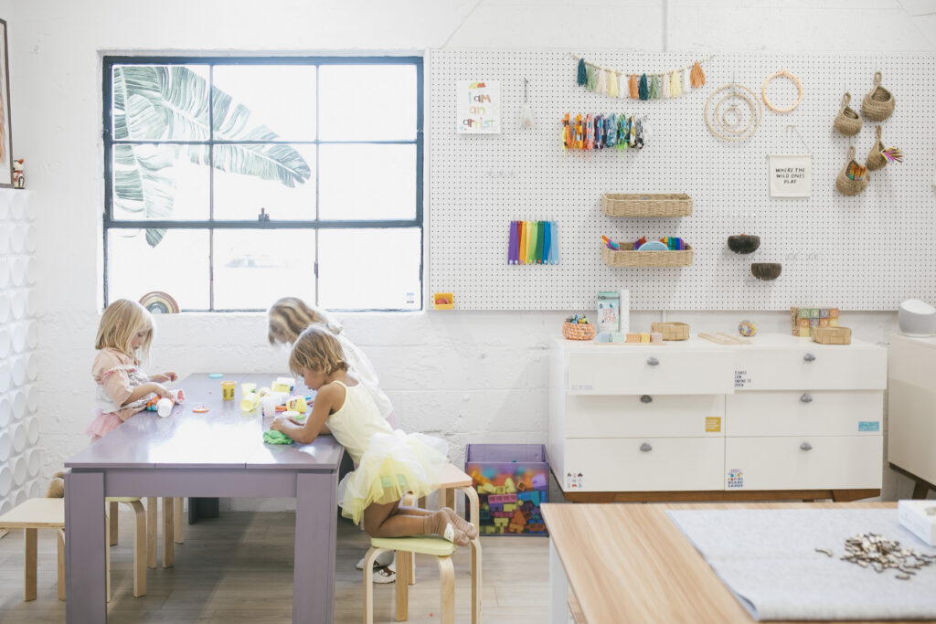 Three little girls are playing at a white table in a white room.