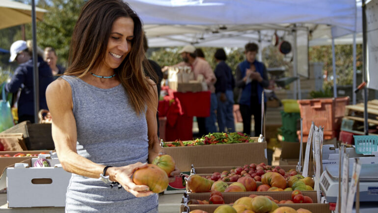 A very fit woman is browsing the fruit stands at a farmer's market.