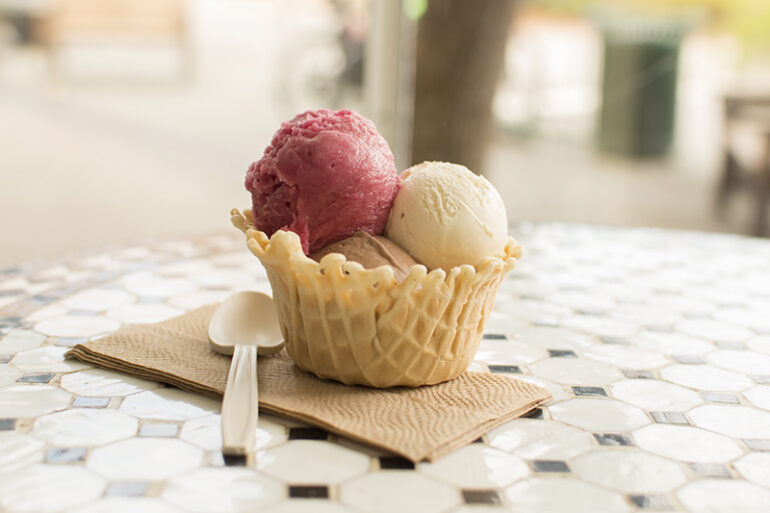 A waffle cup with three scoops of ice cream, vanilla, chocolate and strawberry.