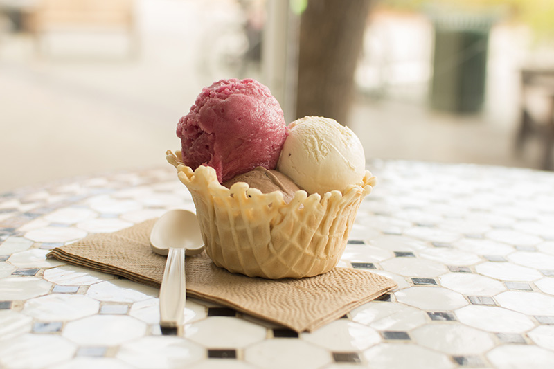 A waffle cup with three scoops of ice cream, vanilla, chocolate and strawberry.