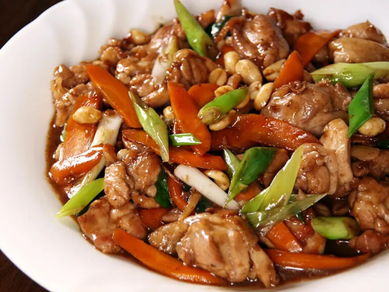 A white plate with chicken, carrots, onions and sauce.
