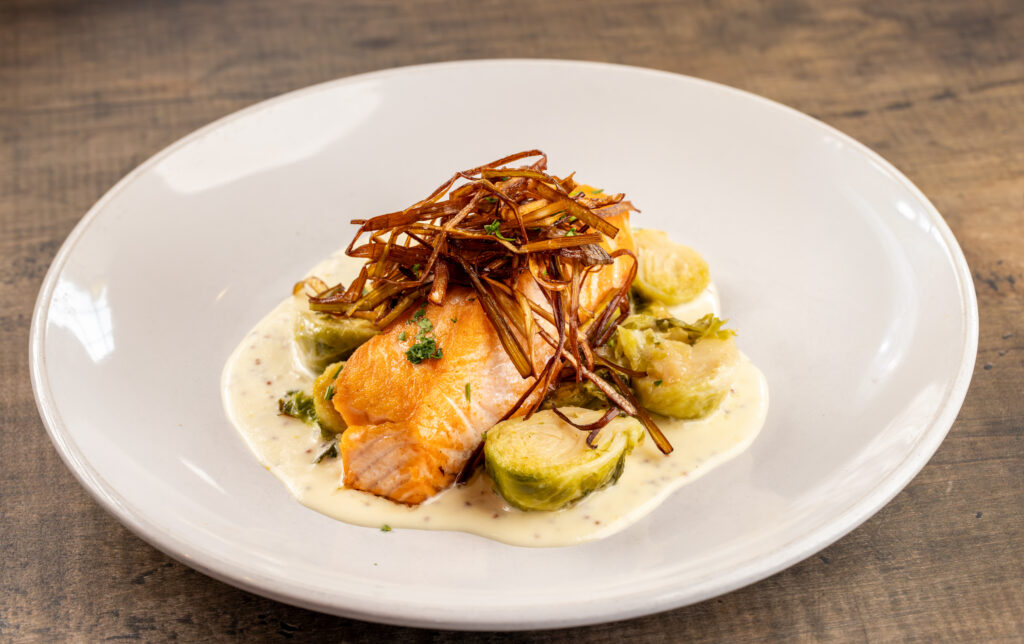 A white dish with a piece of salmon and garnish with cream and vegetables.