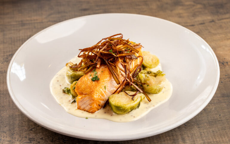 A white dish with a piece of salmon and garnish with cream and vegetables.